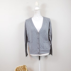 May include: A gray cardigan sweater with a V-neck, long sleeves, and two front pockets. The sweater is buttoned up and displayed on a white mannequin. A woven basket is in the lower left corner.