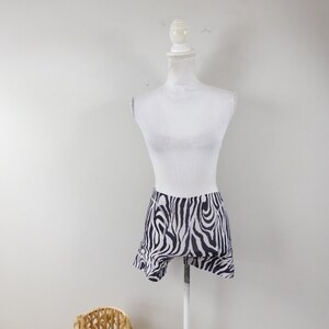 May include: A white mannequin wearing a black and white zebra print skirt. The skirt has a ruffled hem and is made of a lightweight fabric.