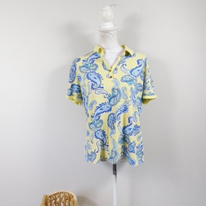 May include: A yellow short-sleeved shirt with a blue paisley pattern. The shirt has a button-up collar and a single button closure.