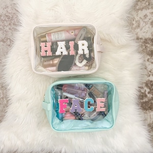 Könnte beinhalten: Zwei transparente, durchsichtige Reißverschlusstaschen mit bunten Buchstaben, die "HAIR" und "FACE" buchstabieren. Die Taschen sind mit verschiedenen Toilettenartikeln und Make-up-Produkten gefüllt.
