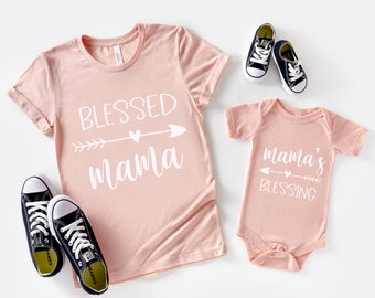 Puede incluir: Un conjunto a juego de camisetas y body para bebé rosas con el texto "Blessed Mama" y "mama's blessing" en blanco. El conjunto incluye un par de zapatillas negras y blancas y un par de zapatillas de bebé.