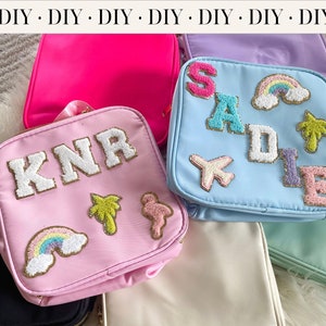 May include: Four personalized cosmetic bags with different names and designs. The bags are made of a soft, light blue, pink, and white fabric. Each bag has a different design, including a rainbow, palm trees, and a flamingo. The bags are perfect for travel or everyday use.