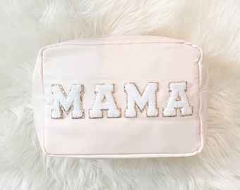 Könnte beinhalten: Eine hellrosa Kosmetiktasche mit dem Wort "MAMA" in weißen Buchstaben mit goldenen Verzierungen.