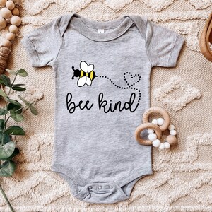 K&ouml;nnte beinhalten: Ein grauer Baby-Strampler mit einem schwarzen und gelben Bienen-Motiv und dem Text "bee kind".