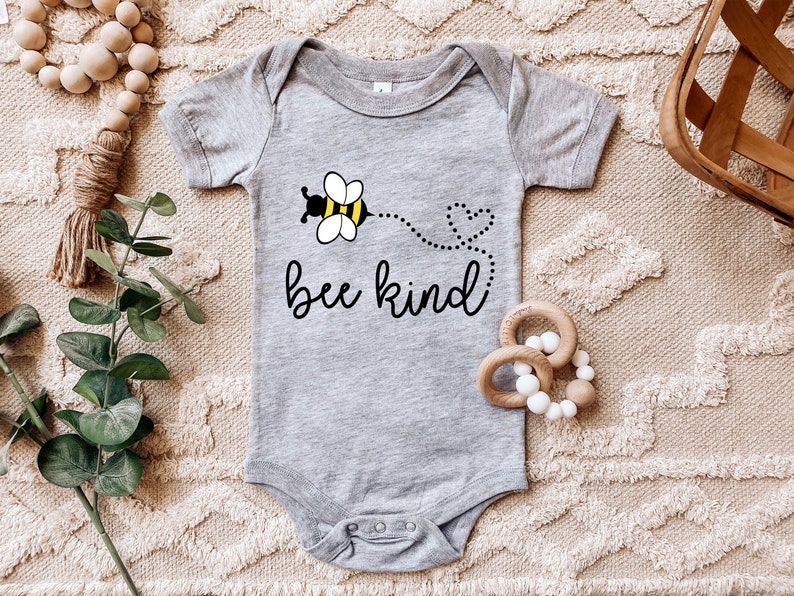K&ouml;nnte beinhalten: Ein grauer Baby-Strampler mit einem schwarzen und gelben Bienen-Motiv und dem Text "bee kind".