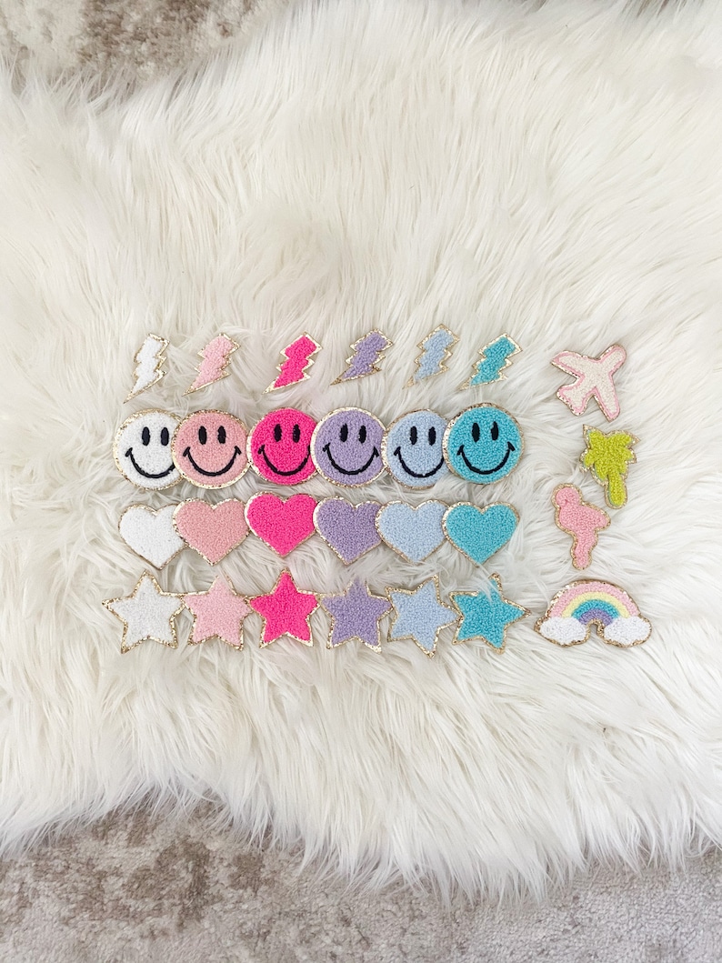 Puede incluir: Colecci&oacute;n de parches coloridos y bordados en varias formas, incluyendo caras sonrientes, corazones, estrellas, rayos y un arco&iacute;ris. Cada parche tiene un borde dorado sobre un fondo blanco y esponjoso.