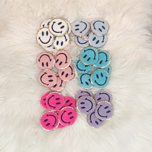 May include: A set of 10 embroidered smiley face patches in various colors, including white, pink, light blue, purple, and hot pink. Each patch has a gold trim and a black smiley face.