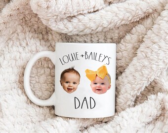 Könnte beinhalten: Ein weißer Keramikbecher mit einem aufgedruckten Design, das den Text "LOUIE + BAILEY'S DAD" in schwarzer Schrift zeigt. Das Design enthält zwei fotografische Porträts von Säuglingen, eines davon mit einer großen gelben Haarschleife, zwischen den Textzeilen.