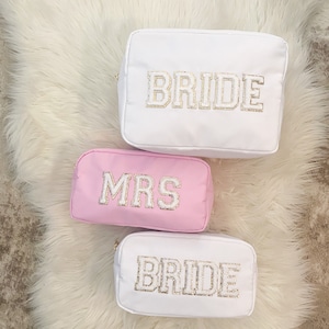 May include: Three white and pink cosmetic bags with gold lettering. The bags say "Bride" and "Mrs."
