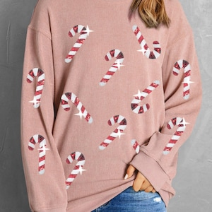 May include: A pink long-sleeved sweatshirt with a Christmas candy cane design. The candy canes are made of red and white sequins.