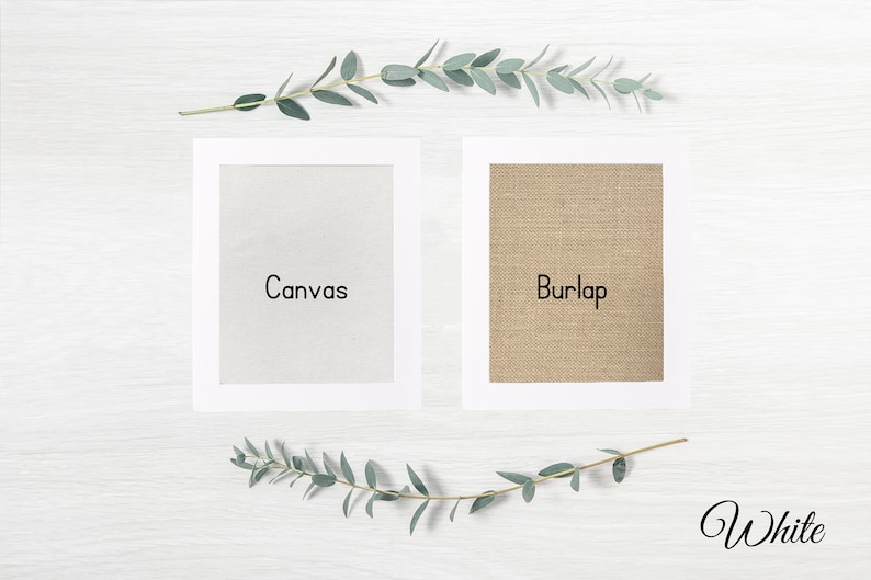 May include: Two framed samples of fabric, one white canvas and one brown burlap, with the words "Canvas" and "Burlap" printed below each sample. The background is a white wooden surface with a sprig of green eucalyptus leaves on either side of the samples.