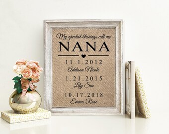 May include: A framed burlap print featuring the black text My greatest blessings call me NANA, followed by three dates and names: 11.1.2012 Addison Nicole, 1.21.2015 Lily Sue, and 10.17.2018 Emma Rose, with a small heart icon below the word NANA.