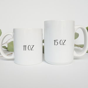 May include: Two white ceramic mugs with black text. The smaller mug is 11 oz and the larger mug is 15 oz.