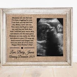 May include: A rectangular wooden frame with a weathered finish containing a burlap background. On the left, black text reads: Mommy, can you feel me? I've been wiggling for you. Love, Baby James Arriving December 2021. On the right is a black and white ultrasound image.