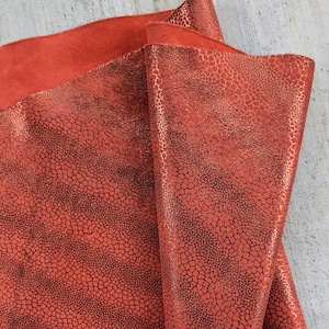 May include: Red leather fabric with a textured, black, reptile-like pattern. The fabric has a slight sheen.