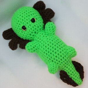 May include: Green crocheted axolotl plush toy with brown details and black eyes.