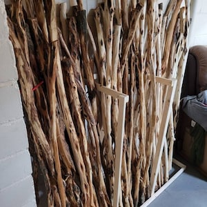 May include: A collection of wooden walking sticks, leaning against a wall, with a variety of knots and textures. The sticks are arranged in a vertical pattern, creating a rustic and natural aesthetic.