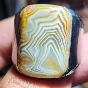 May include: A ring with a white and yellow agate stone set in a silver band. The stone has a swirling pattern of white and yellow.