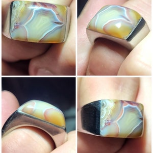 May include: A silver ring with a large, rectangular, multi-colored agate stone. The stone has shades of brown, yellow, white, and red.