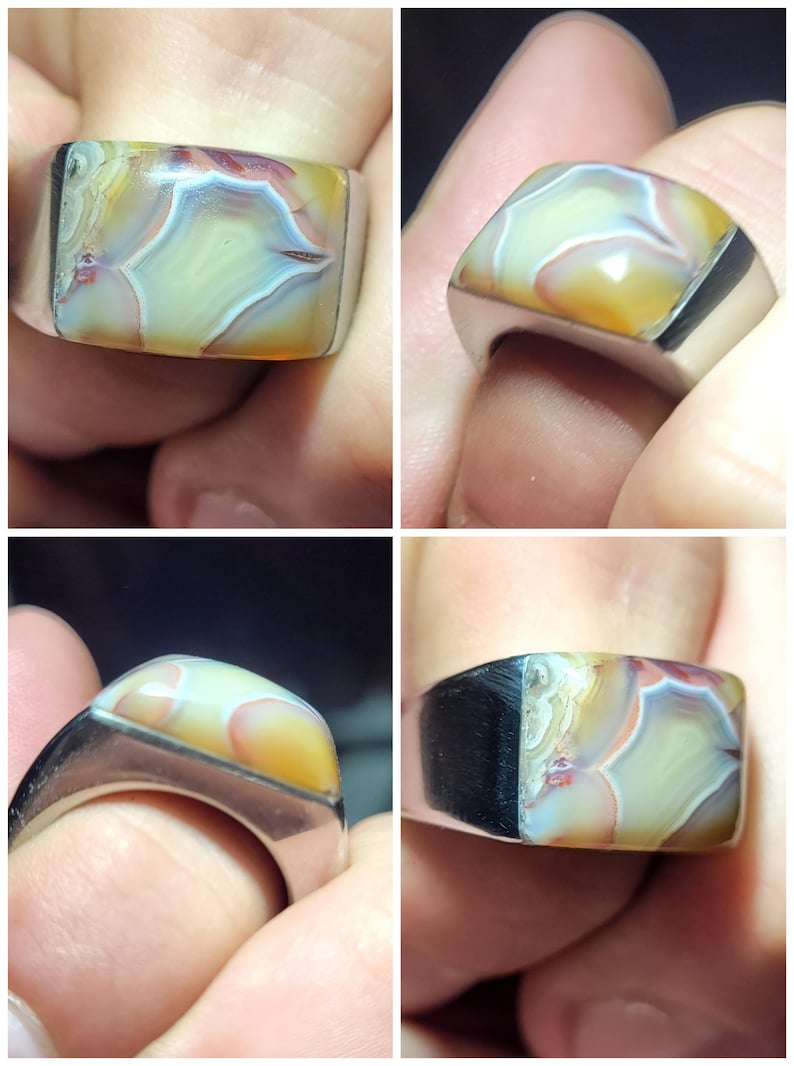 May include: A silver ring with a large, rectangular, multi-colored agate stone. The stone has shades of brown, yellow, white, and red.