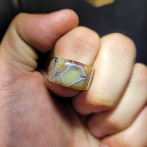 May include: A silver ring with a square-shaped agate gemstone. The agate has a swirling pattern of yellow, brown, red, and white.