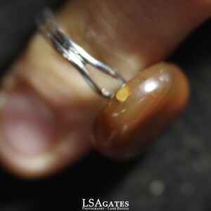 May include: A close-up of a ring with a brown and orange gemstone. The ring is made of silver and has a simple band.