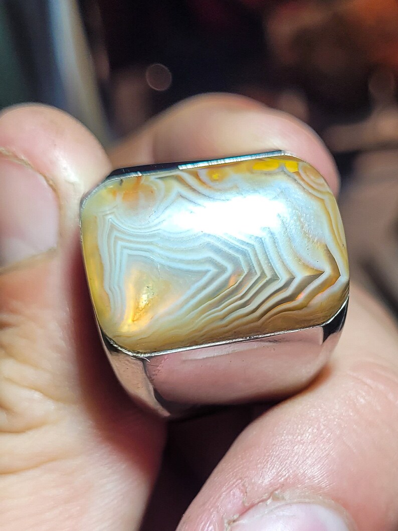 May include: A silver ring with a large, rectangular, agate stone. The stone has a white, brown, and yellow banded pattern.