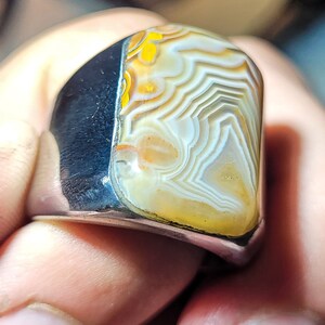 May include: A silver ring with a large, white agate stone set in the center. The stone has a swirling pattern of white, yellow, and brown.