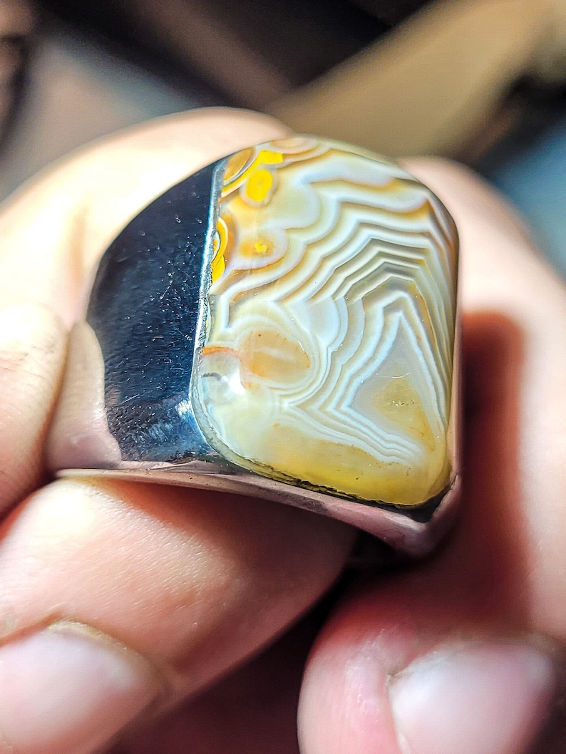 May include: A silver ring with a large, white agate stone set in the center. The stone has a swirling pattern of white, yellow, and brown.
