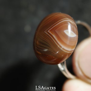 May include: A ring with a brown agate stone. The stone has white and brown stripes and a white center.