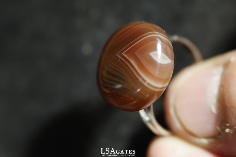 May include: A ring with a brown agate stone. The stone has white and brown stripes and a white center.