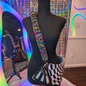 May include: A black and white checkered fabric bag with a rainbow crocheted strap. The bag is hanging on a black mannequin.
