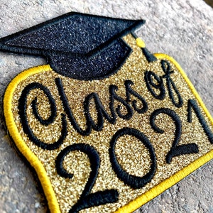 May include: Gold glitter iron-on patch with black embroidery of a graduation cap and the text "Class of 2021".