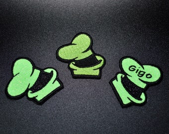May include: Three green felt patches with a black outline, each shaped like a hat with a brim. The top patch has the word "Giggo" written on it.