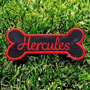 Op de afbeelding: Zwarte en rode hondenbot-patch met de naam "Hercules" geborduurd in rood.
