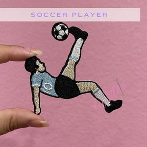 May include: An embroidered patch featuring a soccer player in a light blue jersey, black shorts, and white socks performing a bicycle kick with a black and white soccer ball. The text SOCCER PLAYER is printed in a light purple bar above the patch.