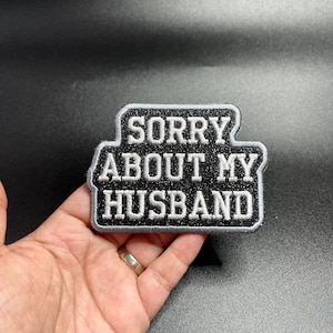 Op de afbeelding: Zwarte strijkpatch met witte tekst die "Sorry About My Husband" luidt.
