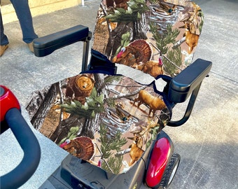 Puede incluir: Un scooter de movilidad rojo y negro con una funda de asiento de camuflaje que presenta imágenes de osos, ciervos y pavos. La funda del asiento está hecha de un tejido suave y de felpa.