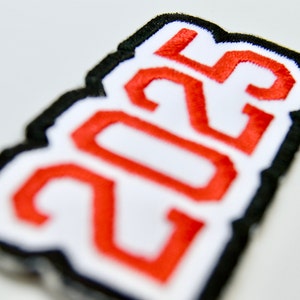 May include: A white patch with a black border and the year 2023 embroidered in red.