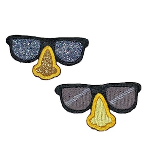 May include: Two embroidered patches featuring black sunglasses with a yellow nose. One pair of glasses has glittery, sparkly lenses, while the other has gray lenses. The patches are likely for clothing or accessories.