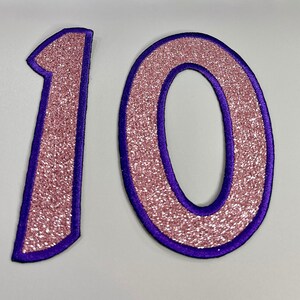 May include: Pink glitter number 10 with a purple outline. The numbers are large and perfect for a birthday party or other celebration.