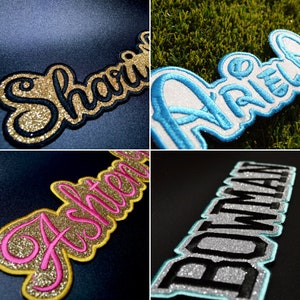 Può includere: Quattro toppe termoadesive con nomi diversi. Le toppe sono realizzate in tessuto con glitter e hanno una combinazione di colori blu, bianco, oro e nero. I nomi sulle toppe sono "Shari", "Ariel", "Ashtien" e "Bowman".