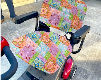 Pode incluir: Um scooter de mobilidade vermelho e preto com uma capa de assento estampada de cores. A capa do assento tem um design de patchwork com cores rosa, verde, azul e laranja.