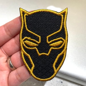 May include: Black and gold embroidered iron-on patch featuring the Black Panther mask.