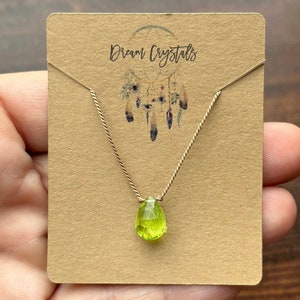 May include: A green peridot gemstone pendant necklace on a gold chain with a brown card that says "Dream Crystals".