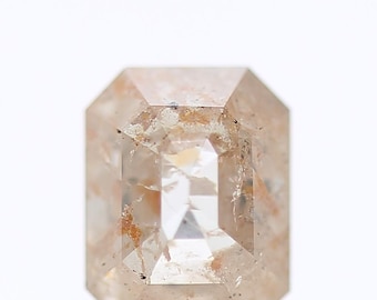 May include: A light brown, rectangular-cut gemstone with internal inclusions. The gem has a clear, reflective centre and a slightly opaque, textured surface. The cut is an emerald cut, with a series of facets.