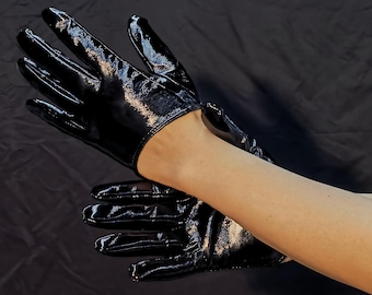 May include: A pair of black patent leather gloves with a shiny finish. The gloves are worn on a person's hands.