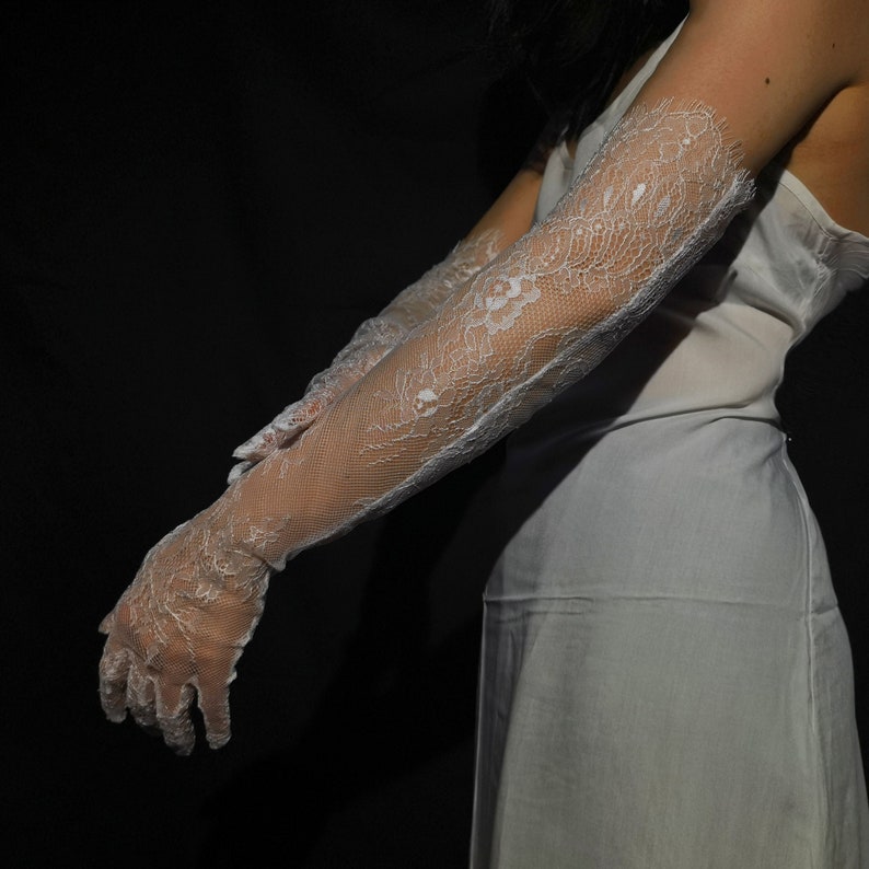 May include: A pair of white lace gloves with a floral pattern. The gloves are long and extend past the elbows.