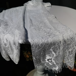 May include: A pair of white lace gloves with a delicate floral pattern. The gloves are made of a soft, sheer fabric and have a scalloped edge.