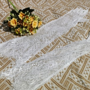 May include: Two white lace gloves on a brown patterned fabric background. The gloves are made of delicate lace and have a soft, feminine look.